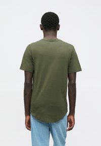 Krátké tričko olivově zelené barvy s kulatým výstřihem a zakřiveným lemem, zobrazené zezadu. Materiál působí měkce a pružně.