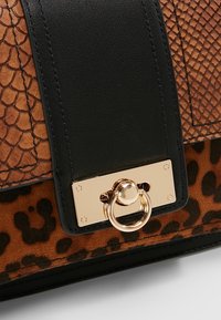 Sac à main en cuir marron avec imprimé serpent et motif léopard, doté d'une bandoulière noire et d'un fermoir doré avec un anneau accent. Surface texturée.