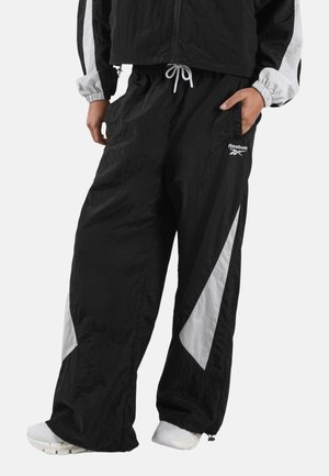 Zwart-witte Reebok trainingsbroek met een elastische taille en een trekkoord, gedragen met een bijpassend zwart-wit jasje en witte sneakers.