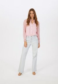 Rosa durchsichtige Bluse mit Spitzenakzenten an den Ärmeln, Knopfverschluss, kombiniert mit hellblauen weiten Jeans und goldenen Riemchensandalen.