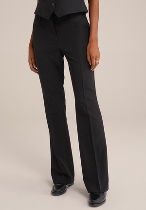 Pantalons noirs ajustés avec un design à jambe droite, présentant un tissu lisse et un subtil éclat, complétés par des chaussures noires.