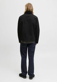 Giacca nera leggera con colletto a punte, design corto e jeans blu a taglio dritto. Scarpe nere con risvolto completano l'outfit.