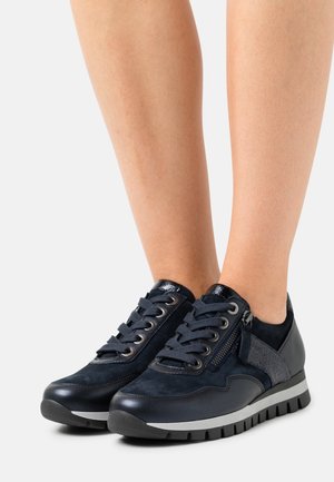 Laivastonsiniset urheilukengät sisältävät mokkaa ja nahkaa, näyttävät nauhat, teksturoidun yksityiskohdan ja mustan kumipohjan hopeisella raidalla.