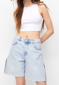Shorts de mezclilla de lavado claro con dobladillos deshilachados, aberturas laterales y diseño tradicional de cinco bolsillos. Combinados con una camiseta crop de canalé blanca.