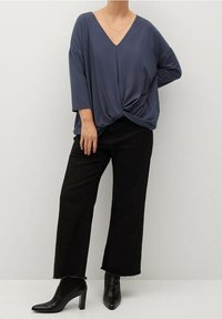 Top blu navy dal taglio morbido con scollatura a V e dettaglio a nodo in vita, abbinato a pantaloni neri a gamba larga e stivaletti neri con tacco.