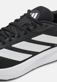Black athletic shoe featuring a mesh upper with white accents, three stripes logo, textured outsole, and a lightweight design.