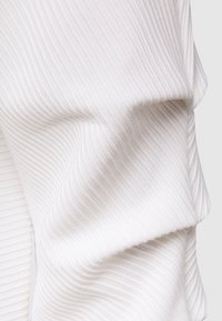 Vit ribbad tyg som draperar och veckar sig, vilket visar en texturerad yta med smala vertikala linjer. Materialet verkar mjukt och något elastiskt.