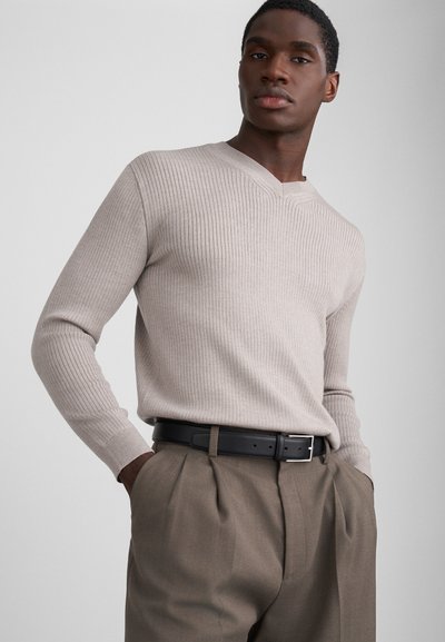 Beige ribbet langærmet sweater med V-udskæring, parret med højtaljede brune bukser og et sort bælte med en sølvspænde.