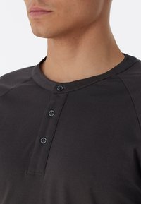 Dunkelgraues kurzärmeliges Henley-Shirt mit Rundhalsausschnitt, das drei schwarze Knöpfe und eine glatte, weiche Textur aufweist.