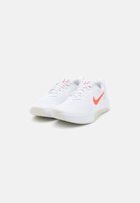 Hvide sportsko med et struktureret mesh-overdel, prydet med et pink Nike-logo på siden, samt en hvid gummisål med et rillede mønster.