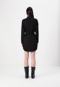 Rochie negre cu mâneci lungi, talie accentuată cu curea, hem curbat și manșete cu nasturi, asortată cu cizme negre până la genunchi cu catarame.