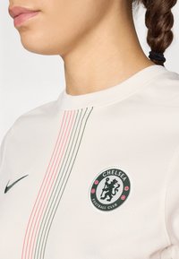 Valkoinen urheilupaita lyhyillä hihoilla. Siinä on vihreät ja punaiset pystysuorat raidat sekä pyöreä Chelsea Football Club -logo rinnassa.