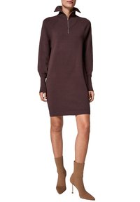 Brązowa dzianinowa sukienka z wysokim kołnierzem i zamkiem błyskawicznym. Długie rękawy i dopasowany krój. Noszona z beżowymi botkami z obcasem typu szpilka.