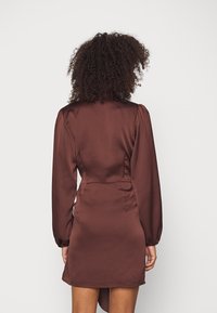 Brun satin klänning med långa puffärmar, inbyggd design och asymmetrisk fåll. Slät textur med en figurnära midja och subtil lyster.