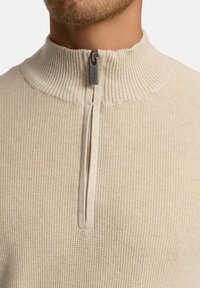 Beige kvart-zip trøje i en tekstureret strik med en ribbet krave, udstyret med en metal lynlås og glat stof under halsudskæringen.