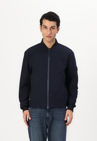 Giacca bomber navy con chiusura a zip, polsini e colletto a coste. Realizzata in tessuto liscio, presenta una patch con logo sulla manica.