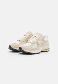 Chaussures de sport beiges avec dessus en suède et mesh, bout rond, semelle épaisse et semelle extérieure noire contrastée. Dotées de lacets crème et de détails logo.