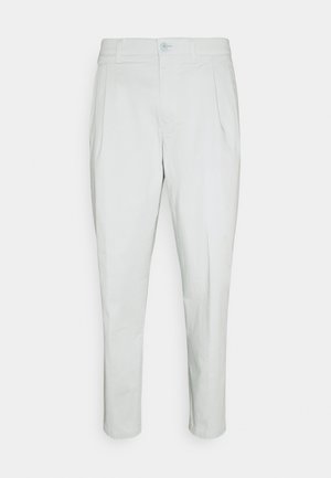 Weiße, zulaufende Hose aus leichtem Stoff, mit einer vorderen Bügelfalte, Knopfverschluss und Gürtelschlaufen. Glatte Textur ohne auffällige Muster.