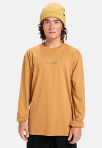 Pitkähihaisessa, sinapinkeltaisessa paidassa on pehmeä kangas ja harmaalla värillä painettu Quiksilver-logo rinnassa. Yhdistettynä samaan sävyyn sopivaan myssyyn.