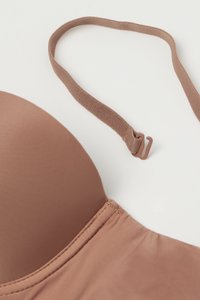 Close-up af en beige bh-skål med justerbar strop og plastik krogspænde på en hvid baggrund.