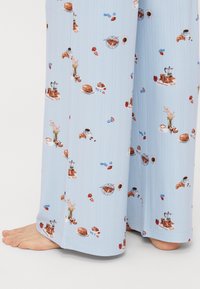 Lyseblå pyjamasbukser med et mad-tema mønster med croissanter, kaffe, pandekager og blomster. Lavet af blødt stof, vidde ben design.