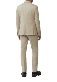 Lichtbeige pak met een subtiele textuur, enkelvoudig gecastreerd jasje en slim-fit broek, gecombineerd met zwarte schoenen. Achteraanzicht van de outfit.