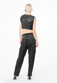 Top corto de cuero negro con un escote alto. Combinado con unos vaqueros negros sueltos que tienen un dobladillo deshilachado y dos bolsillos traseros.