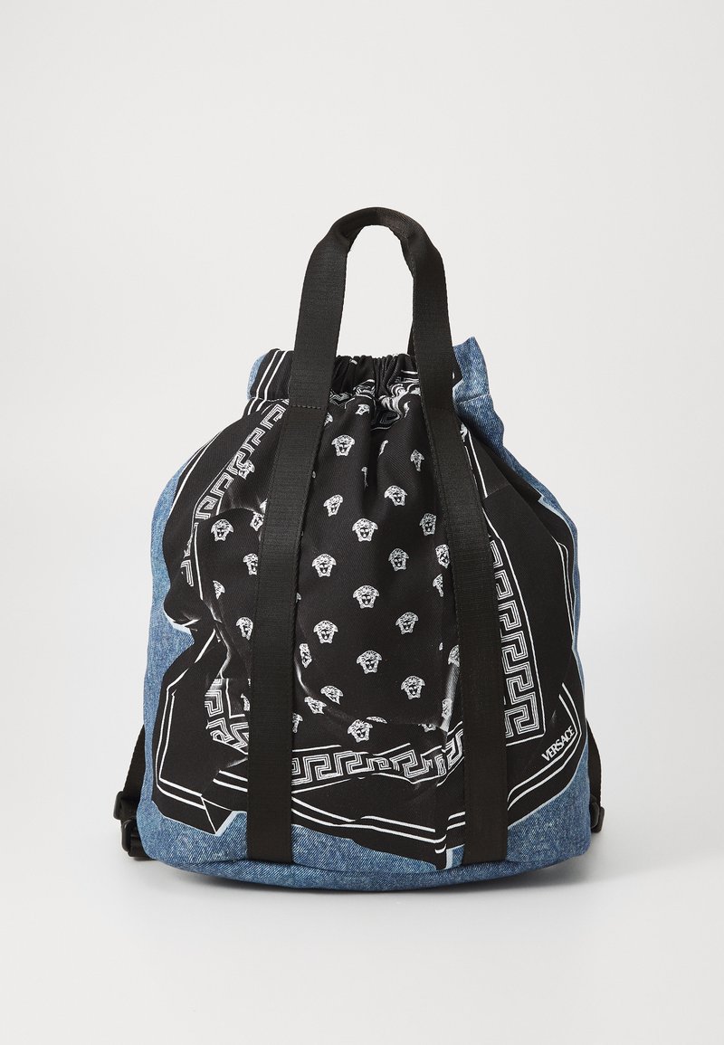 Denim trekzak met een zwart bedrukte bandana bovenkant, uitgerust met zwarte schouderbanden en witte Versace-logo's en accenten.