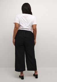 Pantaloni neri a gamba larga con cintura elastica, abbinati a una maglietta bianca a maniche corte, indossati con sandali neri con tacco quadrato.