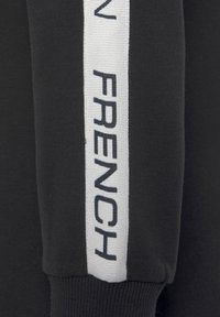 Schwarzer Pullover mit einem weißen gewebten Streifen, der das Wort "FRENCH" in fetter schwarzer Schrift entlang des Ärmels zeigt. Weiche Textur. Lässiges Design.