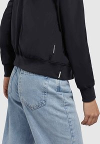 Mustad musta bomber-jakk, millel on elastsed mansetid ja allääre, sile tekstuur ning küljetaskud, koos helesiniste laiade pükstega.