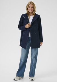 Marineblå uldblandet frakke med bred krave, dobbeltradet knappelukning og sidelommer, parret med lyseblå brede jeans.