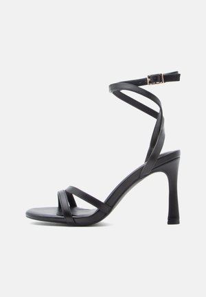 Sandálias de salto alto pretas com um design elegante, apresentando duas tiras estreitas na parte da frente e uma tira cruzada no tornozelo com fivela.