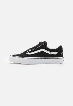 Sort lavtop sneaker med hvid side stribe, hvid gummisål, sorte snørebånd og tekstdetalje rundt om sålkanten på en neutral baggrund.