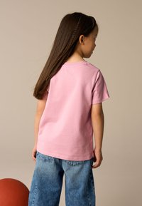 T-shirt in cotone rosa chiaro con maniche corte, scollo tondo e dettagli cuciti, abbinata a pantaloni di jeans blu, vista da dietro.