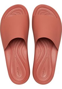 Sandales en plastique rose, fabriquées dans un matériau souple et flexible avec une texture lisse. Le design présente une large lanière et un semelle intérieure à motifs pour plus de confort.