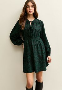 Groene luipaardprintjurk met een trekkoord bij de halslijn, lange pofmouwen en een elastische taille, gemaakt van een gladde, vloeiende stof.