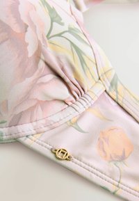 Bloemmotief stof in pastel tinten van roze en geel, met ruches details en een gouden hardware accent.