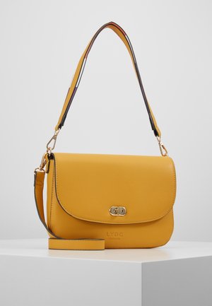 Gul læder crossbody taske med gyldent lås og justerbar multifarvet rem, placeret på en hvid overflade mod en lys grå baggrund.