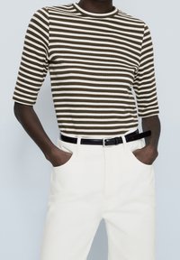 Haut à rayures brunes et blanches à manches courtes avec une texture côtelée, associé à un pantalon blanc et une ceinture noire, présentant des poches latérales.