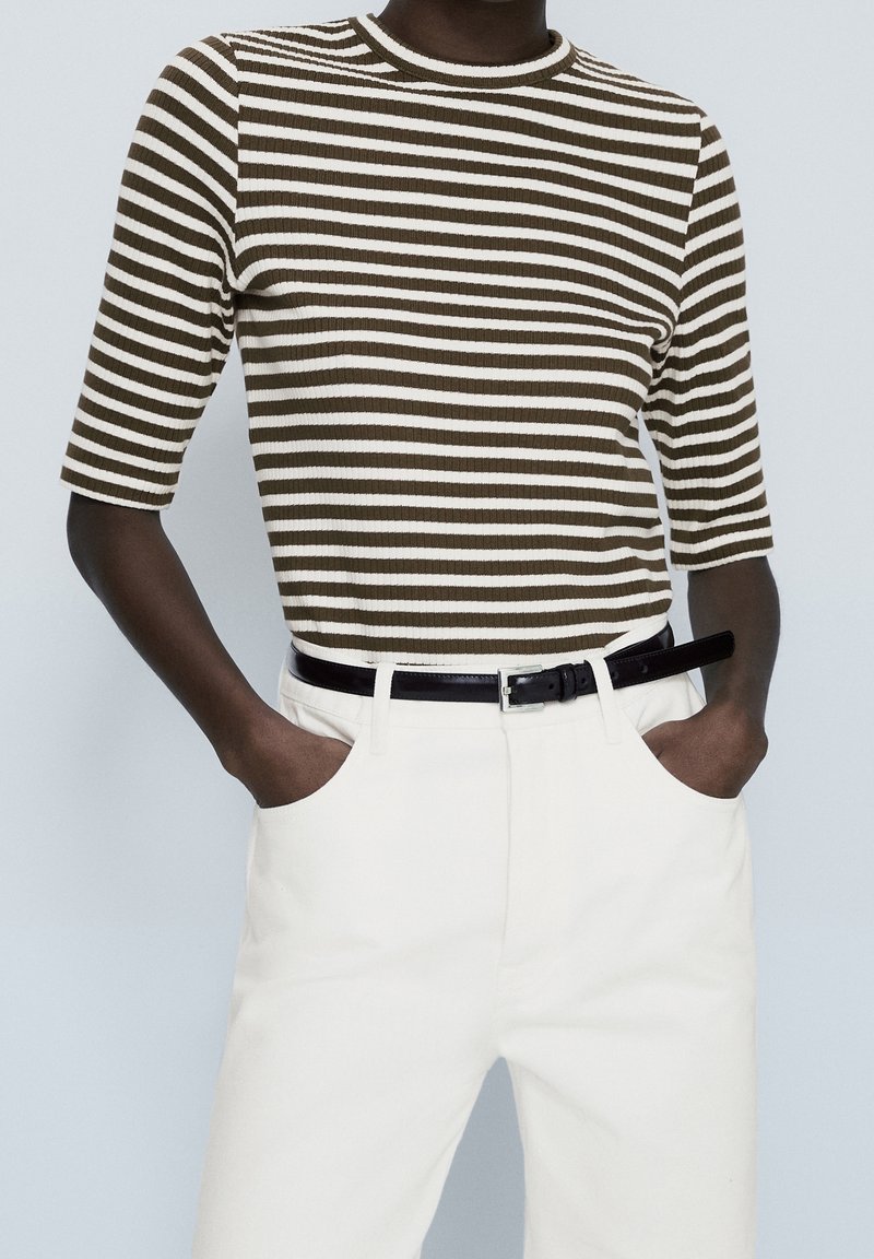 Haut à rayures brunes et blanches à manches courtes avec une texture côtelée, associé à un pantalon blanc et une ceinture noire, présentant des poches latérales.