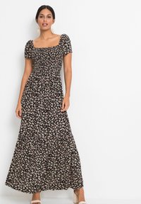 Robe maxi noire à fleurs avec des manches courtes bouffantes, un corsage smocké, une jupe fluide et de petits motifs de fleurs blanches et roses.