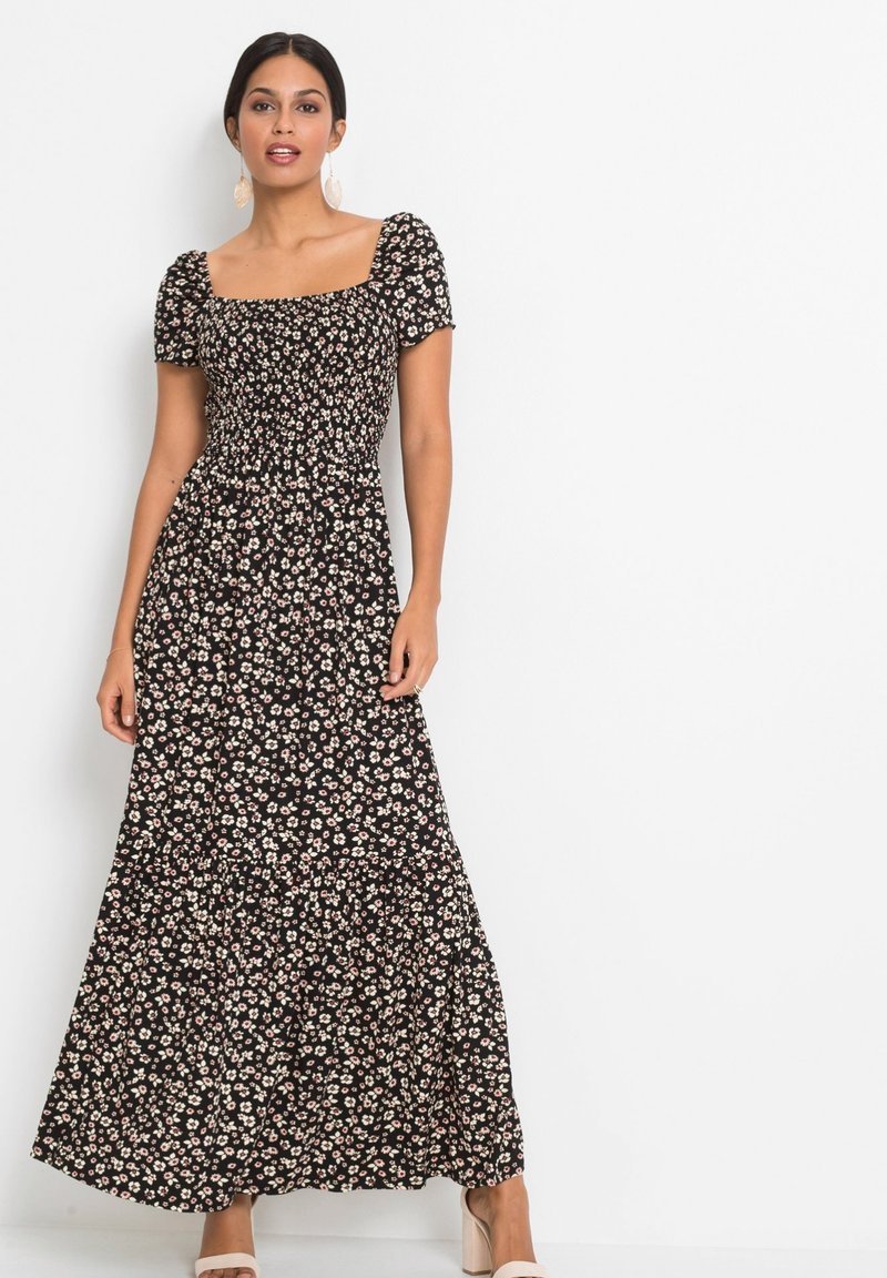 Robe maxi noire à fleurs avec des manches courtes bouffantes, un corsage smocké, une jupe fluide et de petits motifs de fleurs blanches et roses.
