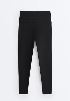Schwarze Leggings mit hoher Taille und nahtlosem Bund, flach auf einem weißen Hintergrund gelegt.