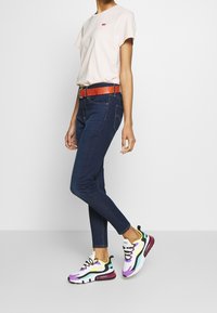 Světle růžové tričko, tmavě modré skinny džíny a vícebarevné tenisky se vzorem v purpurové, žluté a černé barvě. Akcentem je oranžový strukturovaný pásek.