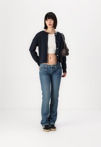Navy blauwe, cropped cardigan met knoopsluiting, gecombineerd met lichtblauwe jeans en zwarte sneakers. Gestructureerde stof en aansluitend ontwerp.