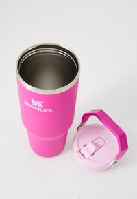 Svetlo roza izolirani tumbler Stanley z notranjostjo iz nerjavečega jekla in usklajenim roza pokrovčkom, postavljenim ob njem na beli površini.