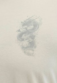 Σχεδίαση ξεθωριασμένου γκρι δράκου με στροβιλιζόμενες λεπτομέρειες, τυπωμένη σε φόντο ελαφρύ μπεζ ύφασμα.