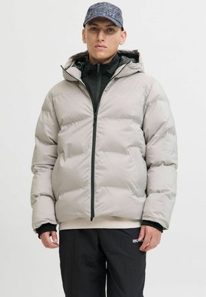 Chaqueta de plumas gris claro con cierre frontal y capucha, que presenta una textura suave y puños acanalados, llevada sobre una camiseta negra y pantalones oscuros.
