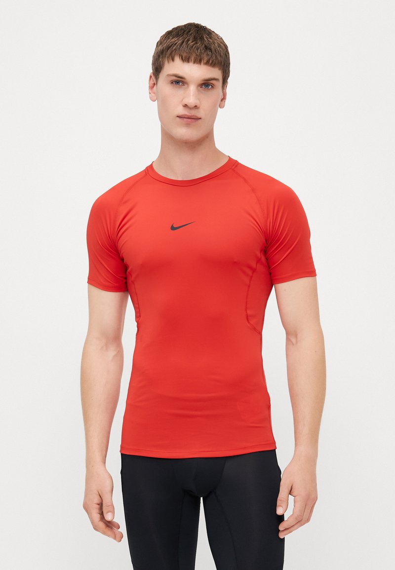 Tricou sportiv scurt cu mâneci, de culoare roșie, fabricat dintr-un material elastic și neted; are un logo Nike negru în centrul său și un guler rotund.